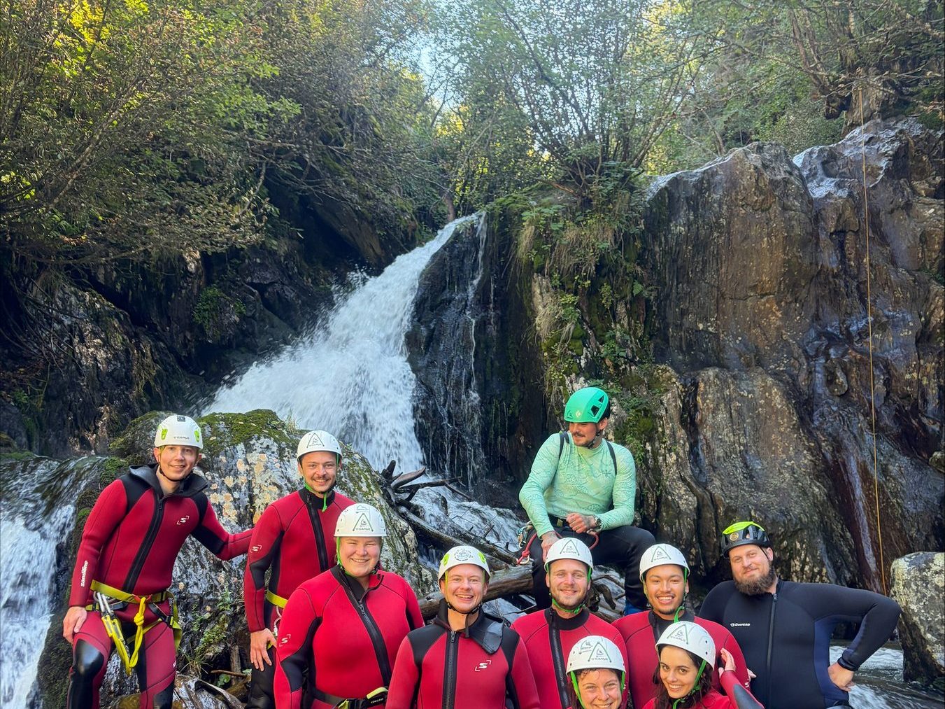 Group in red wetsuits standing together in front of a waterfall in the canyon