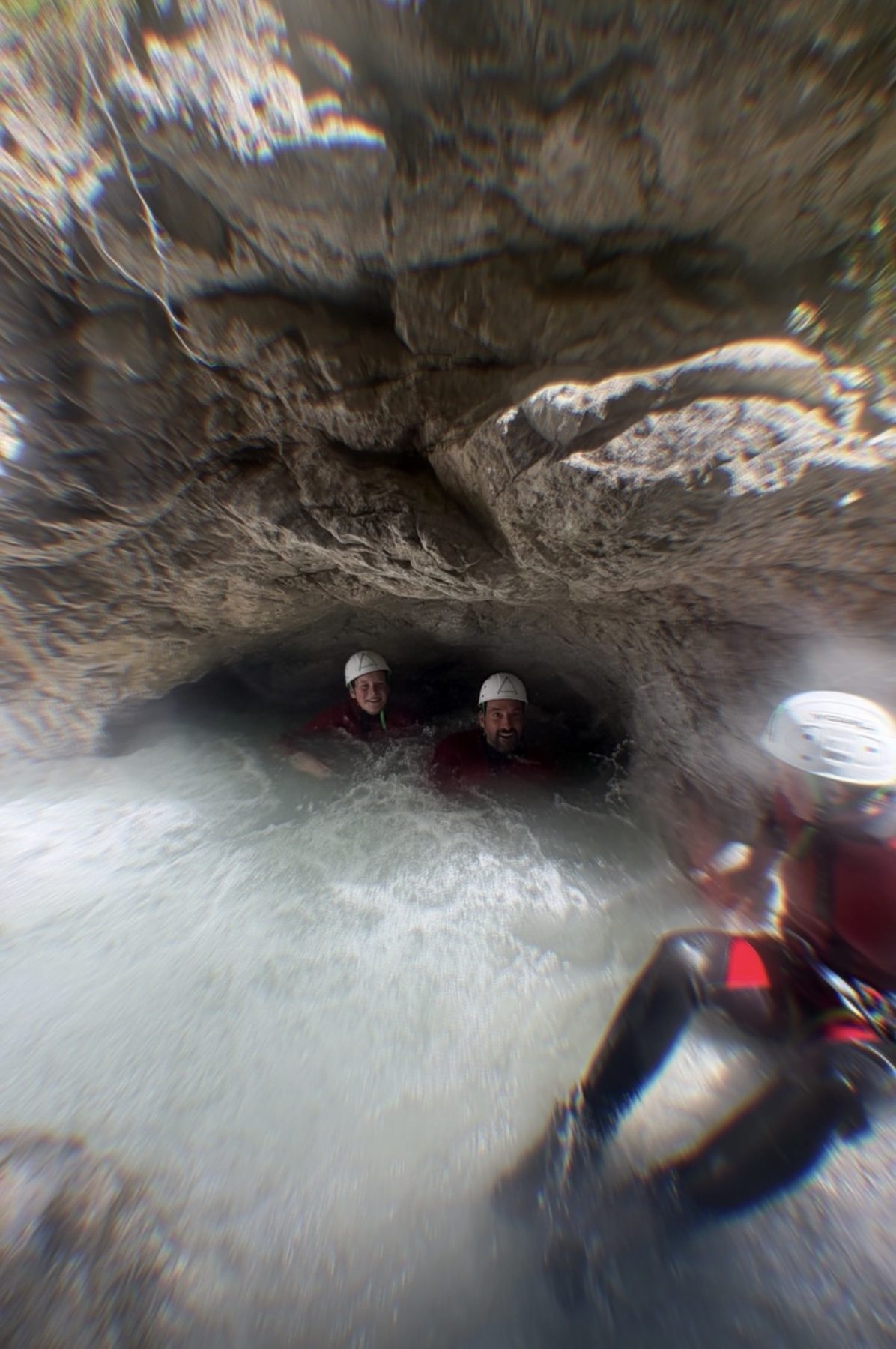 Zwei Personen rutschen durch eine schmale, ausgewaschene Felsrinne ins Wasser