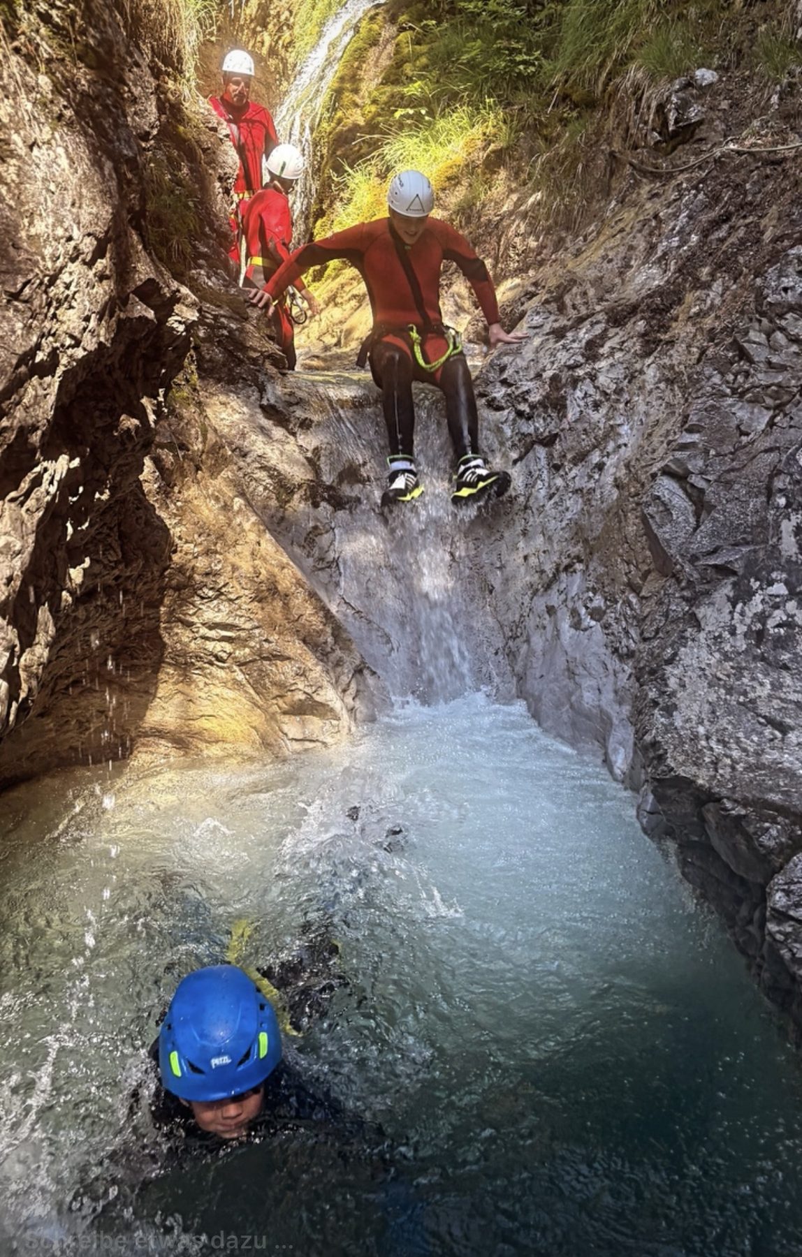 Person mit blauem Helm schwimmt in einem türkisfarbenen Becken zwischen Felswänden