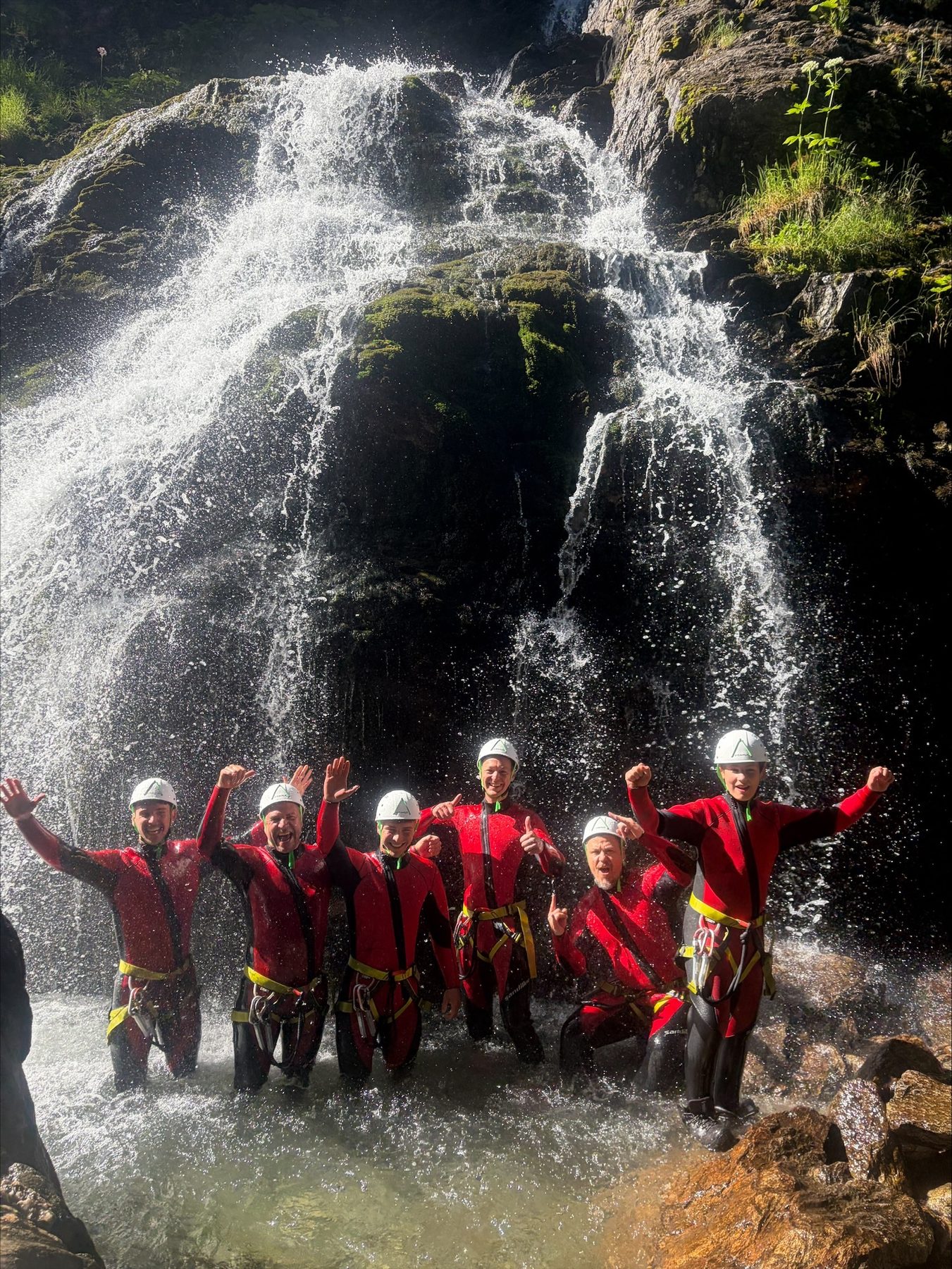Gruppe steht am Fuß eines hohen, mehrstufigen Wasserfalls im Wald