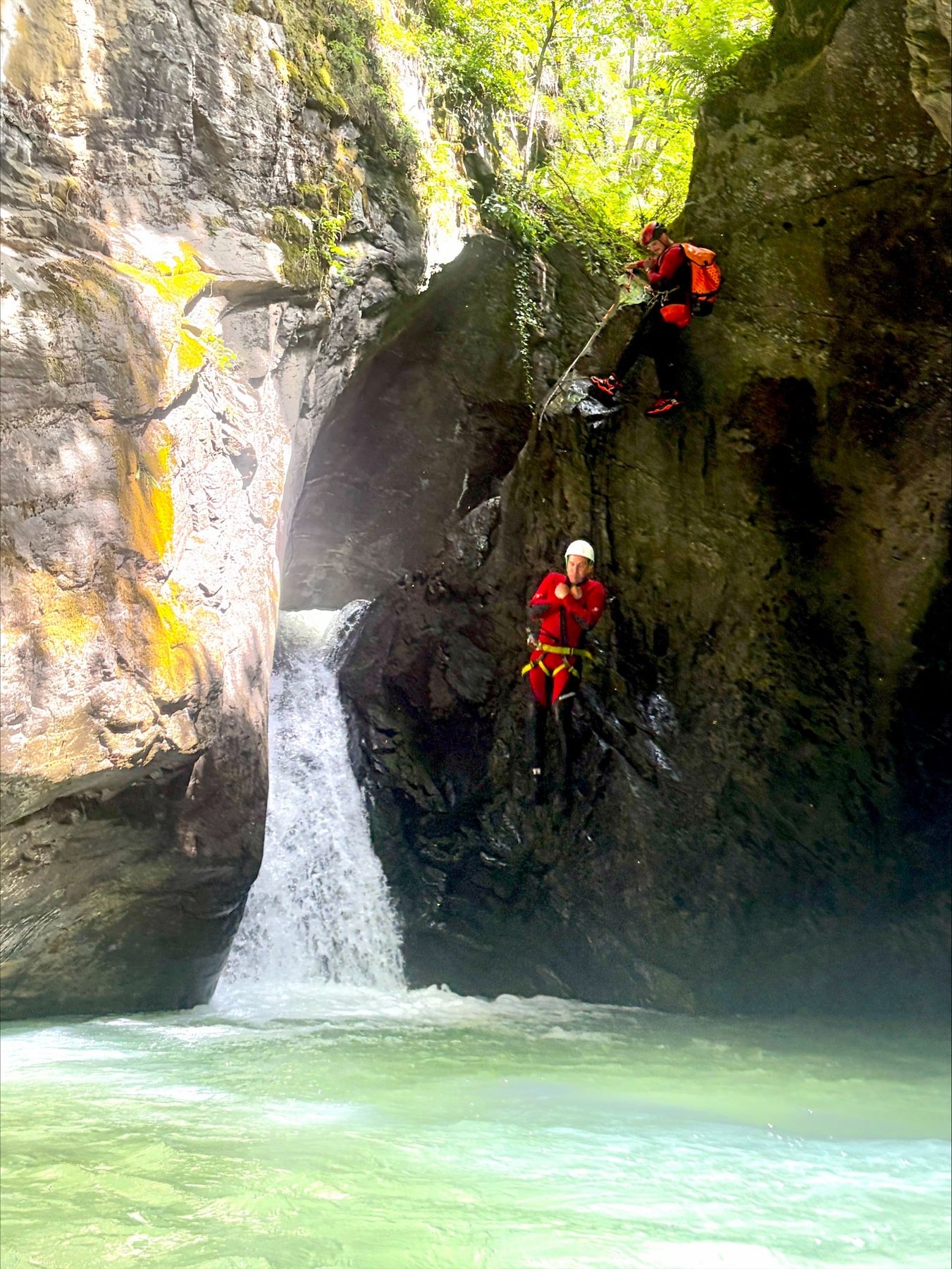 Zwei Personen seilen sich nacheinander an einem hohen Wasserfall ab