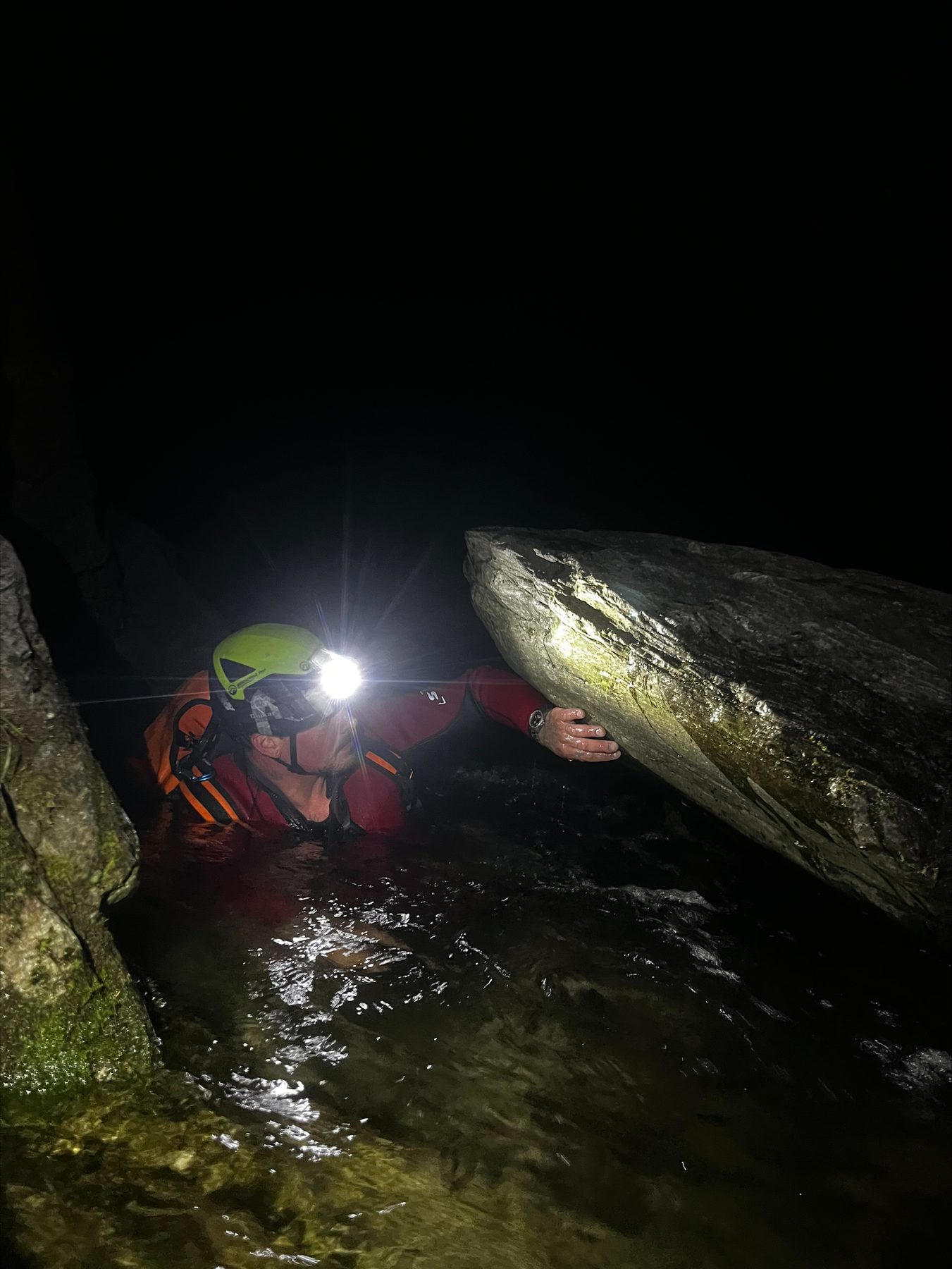 Stirnlampenlicht spiegelt sich nachts auf dem Wasser einer dunklen Schlucht