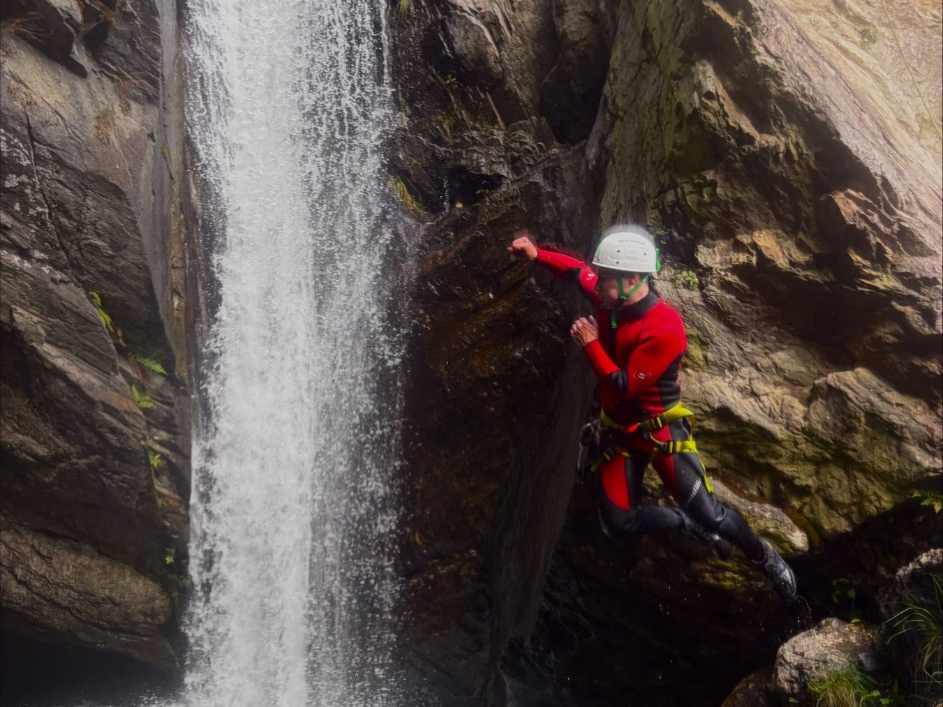 Person springt neben einem hohen Wasserfall von einer Felskante in ein Becken