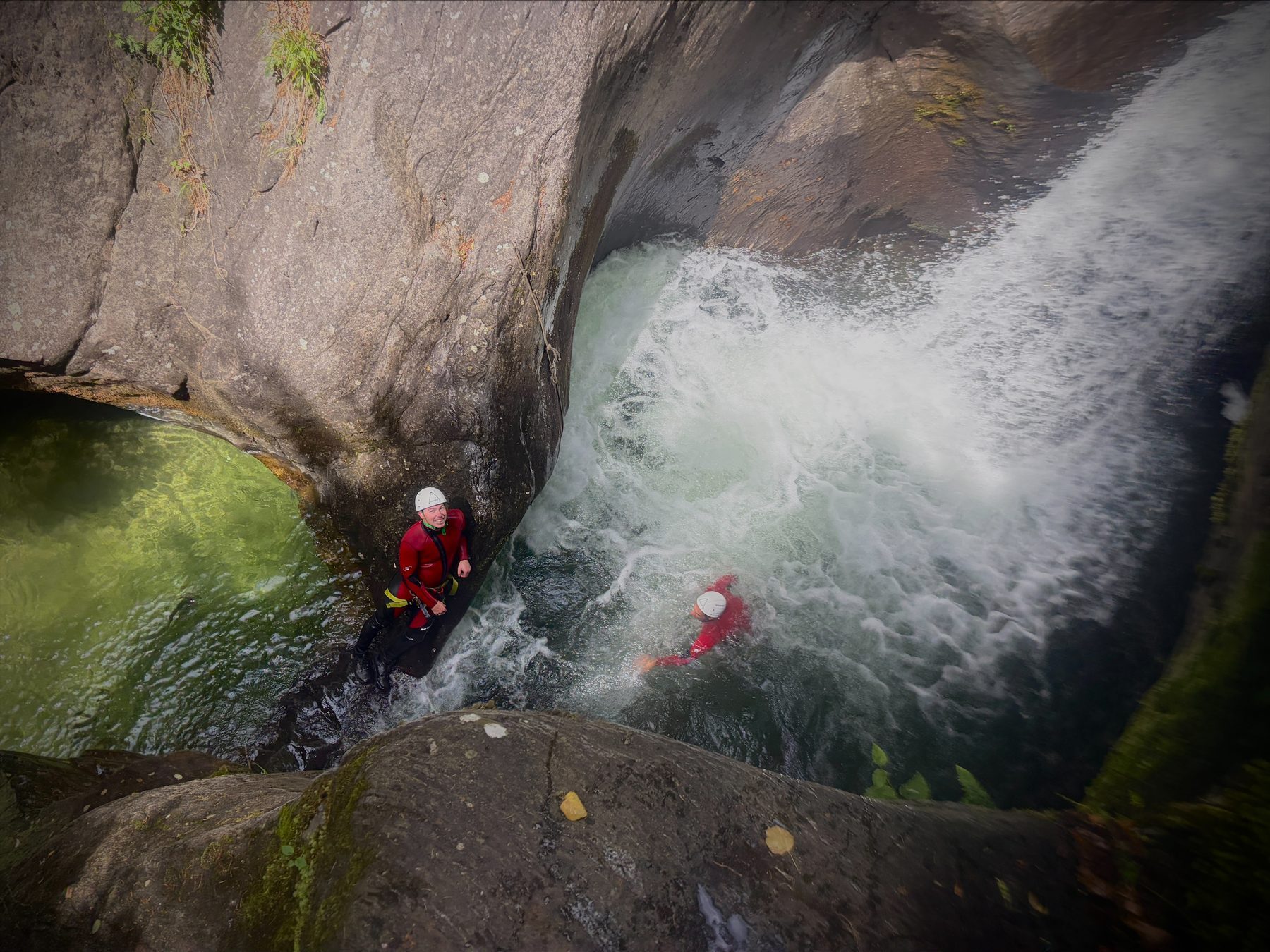 Person rutscht über eine große Felsstufe in ein tiefes Becken der engen Schlucht