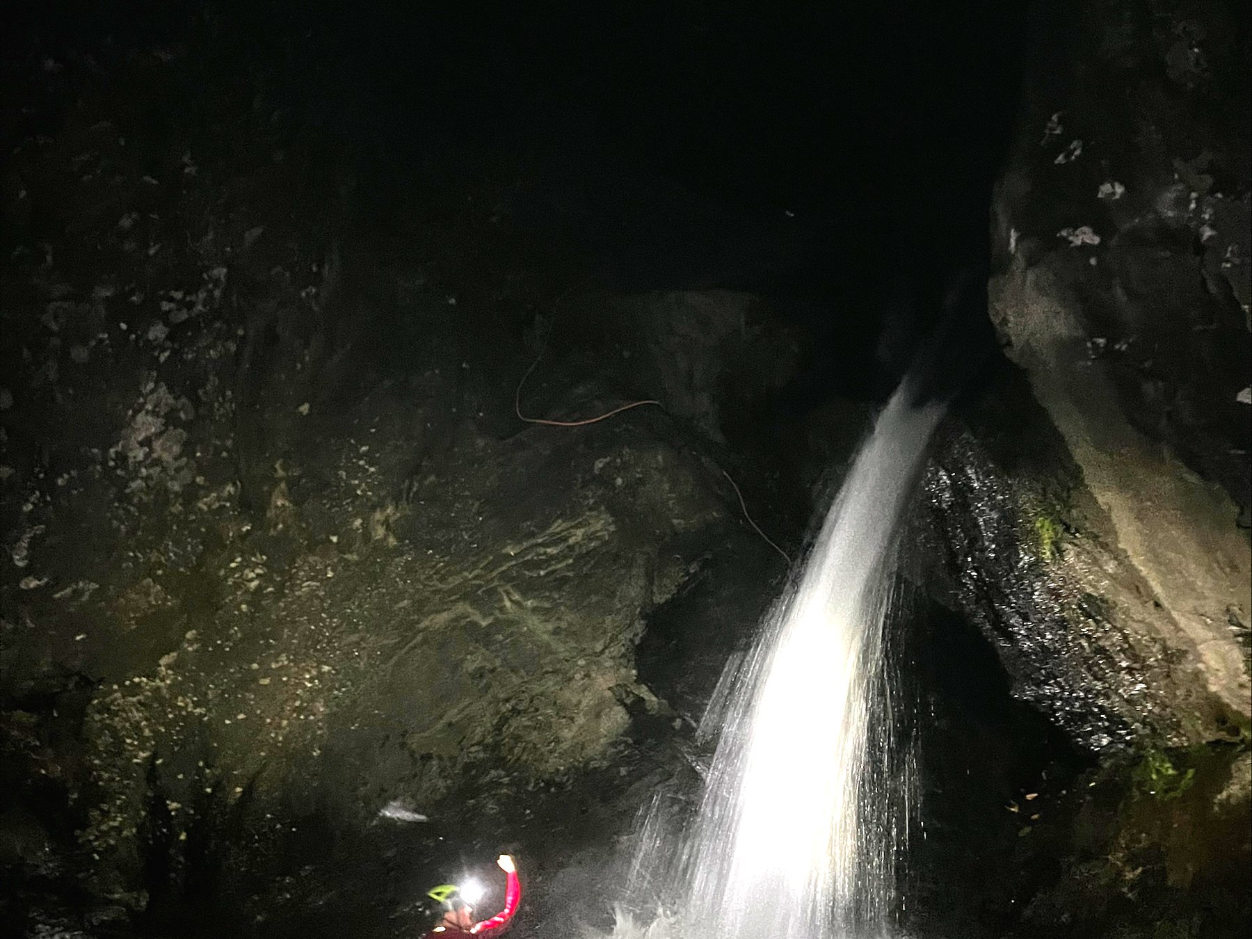 Person im Scheinwerferlicht neben einem Wasserfall in völlig dunkler Schlucht