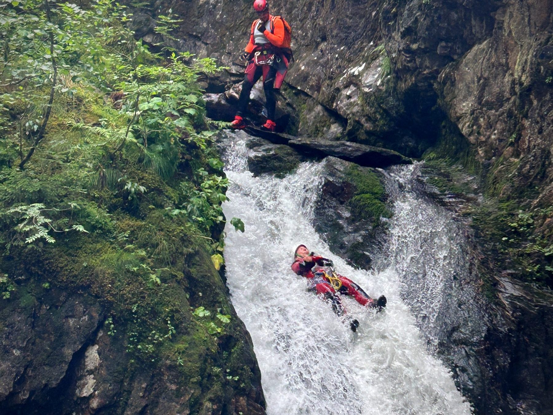 Person gleitet über eine natürliche Wasserrutsche, eine weitere sichert von oben