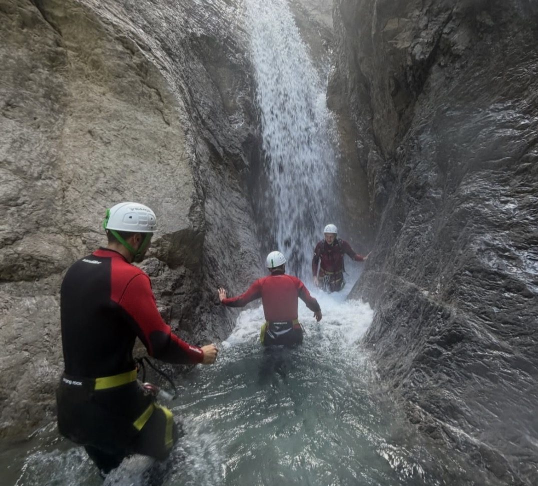 Zwei Personen stehen unter einem schmalen Wasserfall in einer engen Felsspalte