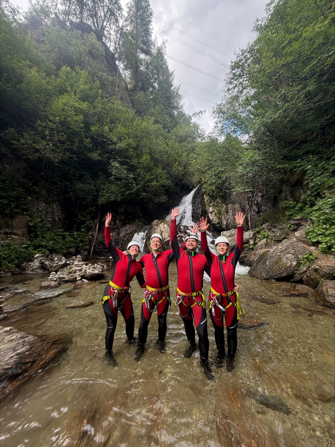 Gruppe in Neoprenanzügen steht im Flussbett und streckt die Arme in die Luft